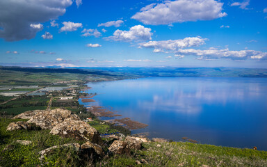 Fototapeta na wymiar Beautiful view of the Sea of Galilee from the cliff of Mount Arbel National Park and Nature Reserve, with clouds in the sky and snow-capped Mt Hermon in the distance; Lower Galilee, Israel
