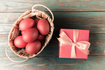 Pink Easter eggs in basket and gift box on rustic wooden background