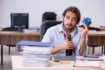 Young male employee drinking alcohol in the office