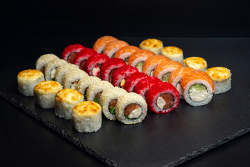 Japanese food, set of baked rolls, rolls in white sesame, red tobiko caviar, Philadelphia with curd cheese on a black slate board