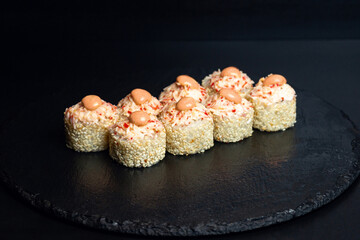 Japanese food, spicy rolls in white sesame seeds with spicy sauce on a black background