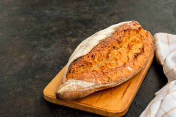 A whole loaf of homemade wheat bread on a wooden board against a dark concrete background.
