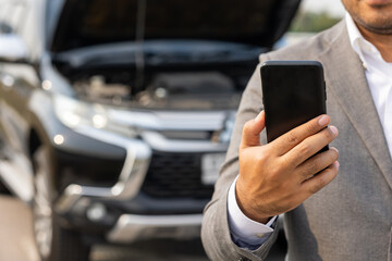 Young asian business has broken down car. He open hood and check the engine. He using smartphone call for help and service. Car broken on the side of the road