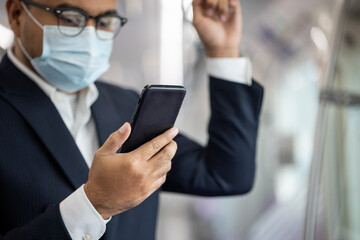 Young asian businessman wearing protection mask using smartphone hold the handrail in skytrain. Businessman in urban city travel by sky train.