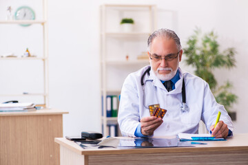 Old male doctor writing prescription in the clinic