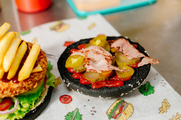 The process of making a chicken burger with fries in a black bun. The chef prepares a chicken burger with fries. Cooking burgers in the diner kitchen.