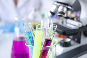 Multi-colored test tubes with liquids stand next to microscope