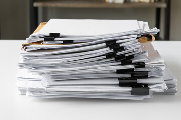 Piles of white papers work large piles of papers stacked together. On the desk in the office with black clip. Documents that are not finished. Business concept.