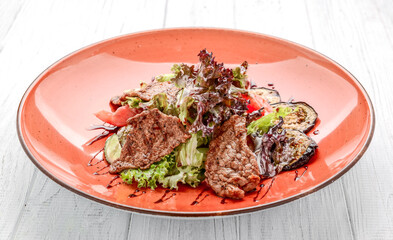 Pork meat grilled with fresh vegetable salad on a white plate.