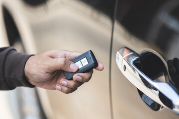 Close up male hand holding car key. Man unlock car door by remote key push button near car door.