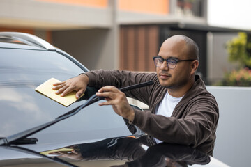 Young asian man uses a microfiber cloth and polish to wipe the front mirror car to make them shine He takes care of every detail of the car mirror.