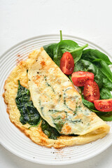 Omelet or omelette with spinach, cherry tomato and pepper seasoning on a white plate, on white background. Top view.