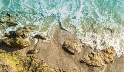 Sand beach seaside top view with white foamy wave on the beach and rock 