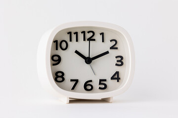 Small white alarm clock, black numbers, set the time for 10.10 o'clock, placed on a white table.