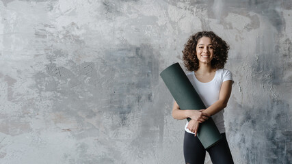 Young african american woman standing with exercise mat in fitness center