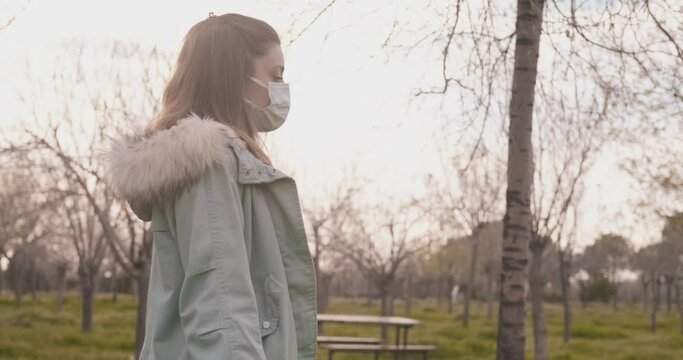 Young woman is walking on forest, autumn time with face mask. Protective medical wearing in holiday time.