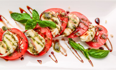 Caprese salad with mozzarella, tomato, basil and balsamic vinegar arranged on white plate