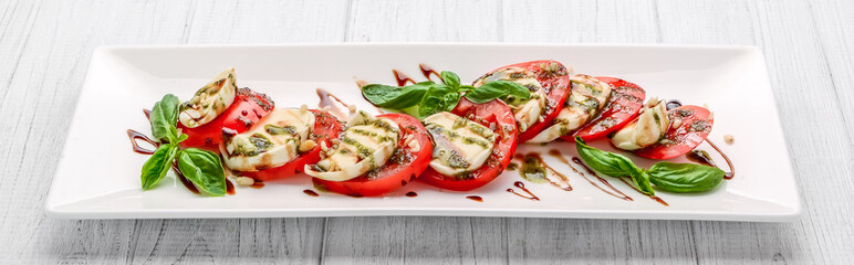 Caprese salad with mozzarella, tomato, basil and balsamic vinegar arranged on white plate