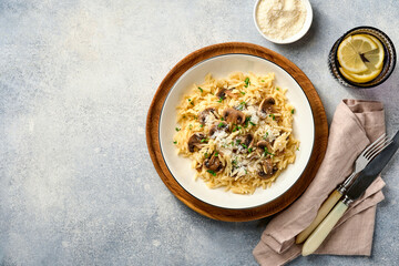 Dining italian pasta risoni, mushrooms, sauce, Parmesan, thyme, garlic, olive oil, in white plate over slate, stone or concrete background. Top view with copy space. Italian cuisine.