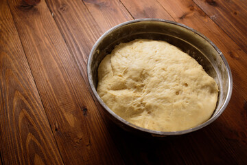 Raw yeast dough resting and rising in large metal bowl on dark wooden background.