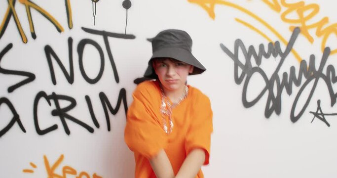 Teenage boy enjoys rap music make yo gesture shakes hands moves with rhythm of music dressed in fashionable clothes poses against colorful graffiti wall. Urban style youth subculture and lifestyle
