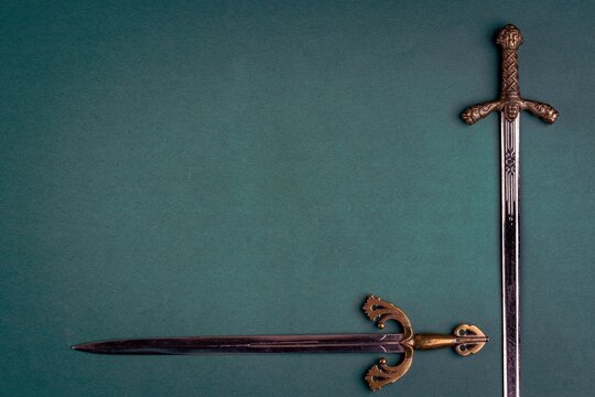 Two old knightly swords on a green velvet background. Copy space