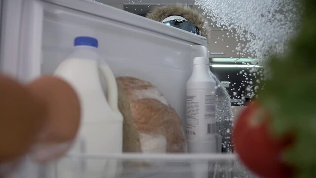 Beautiful girl in winter clothes opens her refrigerator with food and snow falls on her. Super slow motion