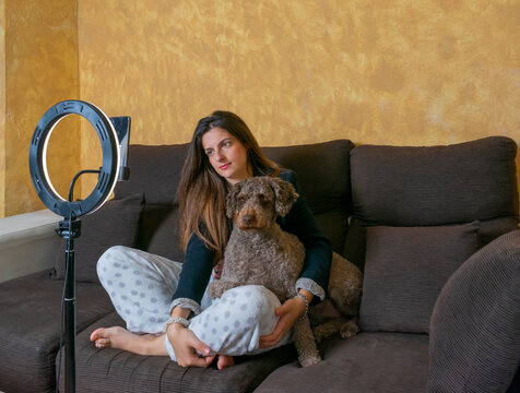 mujer haciendo videoconferencia con su móvil para una Reunión de trabajo en casa, sentada en el sofá teletrabajando con su perro haciendole compañia
