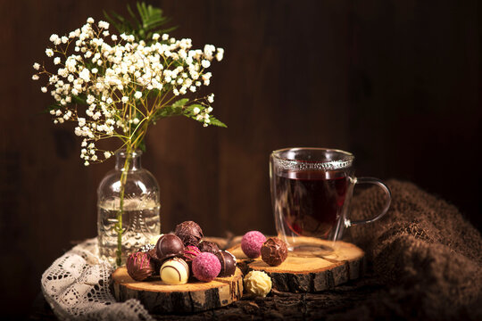Teezeit in rustikal Still. Schleier Kraut liegt als Deko auf dem Holztisch. Glas  Tee steht auf dem Holzhintergrund, bunte Pralinen liegen liegen auf dem St&uuml;ck Holz