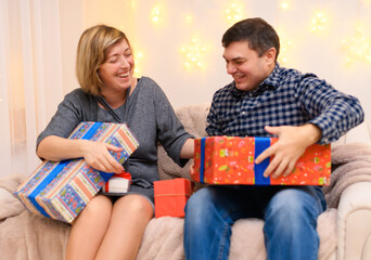 portrait of adult romantic couple, sitting with gifts on a couch at home, holiday lights on a wall