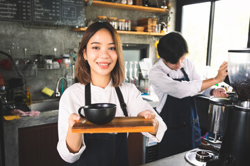 Two asian coffee waitress making cup of hot coffee latte in coffee shop cafe. Barista working with coffee machine in shop.