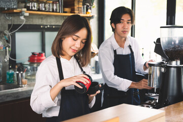 Two asian coffee waitress making cup of hot coffee latte in coffee shop cafe. Barista working with coffee machine in shop.