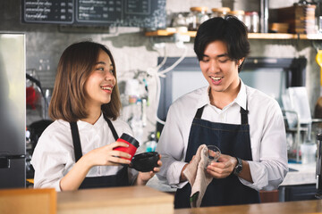 Two asian coffee waitress making cup of hot coffee latte in coffee shop cafe. Barista working with coffee machine in shop.