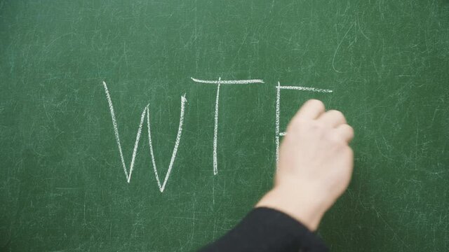 Male hand writing word wtf with chalk on blackboard or green chalkboard in classroom