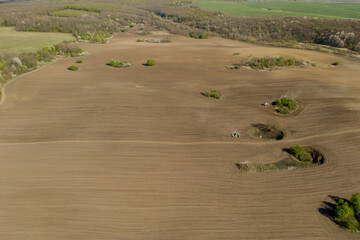 Obraz premium Aerial view large tractor cultivating a dry field. Top down aerial view tractor cultivating ground and seeding a dry field. Aerial tractor cuts furrows in farm field for sowing