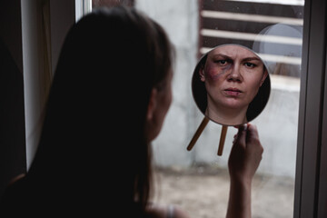 Domestic violence, abuse woman with bruise on face by the window looks in the mirror