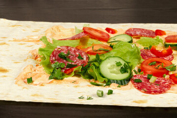 ingredients for shawarma are laid out on a thin pita bread. tomatoes, greens, salami, cheese, cucumber and lettuce close-up