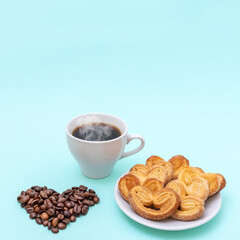Steaming coffee cup, heart shaped cookies, heart shaped coffee beans on a blue background, copy space