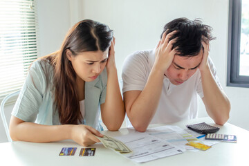 stressed young couple holding credit card and worried about family budget expense cost bills and calculator on desk in home, plan money cost saving, investment, business finance and expenses concept