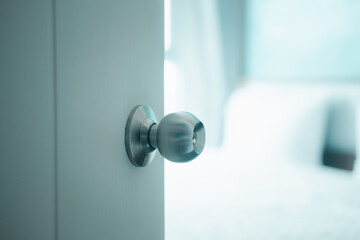 White door with handle opening through bedroom. Door half opened on blurred bedroom background.