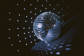 Illuminated by sun light silver disco mirror ball. Dark black background and cold blue and purple shadows. Party classic decoration. Boho style decor
