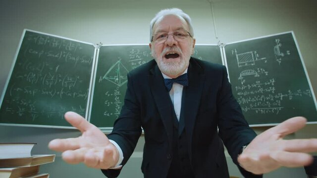 Emotional Eccentric Teacher Trying Explain Mathematical Formulas Written In Chalk On Chalkboard In Classroom. POV View Funny Senior Professor Emotionally Speaking To Pupil Who Does Not Understand Math