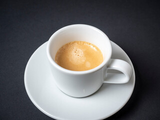 Naklejka premium a white coffee mug with a full espresso is set on a saucer and on a black background. Coffee, energy drink. Delicious foam