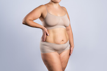 Fat woman in beige underwear on gray background, overweight female body