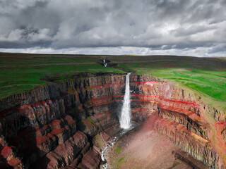 Aerial drone view of Hengifoss waterfall landscape in Iceland. Red layers of clay between basaltic...