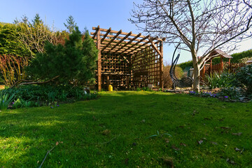 Wooden garden gazebo with openwork walls and an early spring lawn in the garden 
