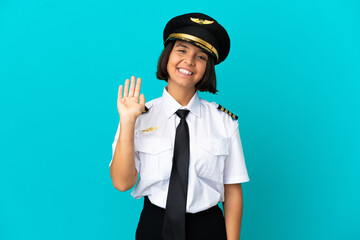 Young airplane pilot over isolated blue background saluting with hand with happy expression