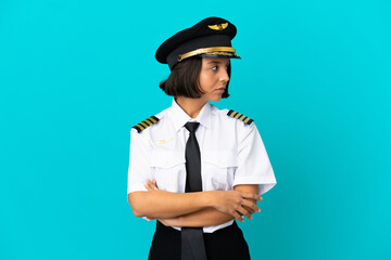 Young airplane pilot over isolated blue background keeping the arms crossed