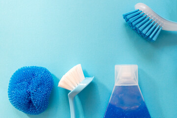 Blue monochrome flay lay of cleaning tool set with copy space in the left corner. Brushes, spray, bottles, sponges.