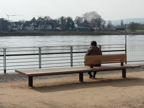 a woman seen from behind, sitting on a bench at the quayside of the Rhine - symbol for loneliness in times of the Corona pandemic